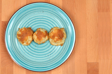 Three cooked potato dumplings topped with toasted breadcrumbs on a blue plate, set on a wooden surface