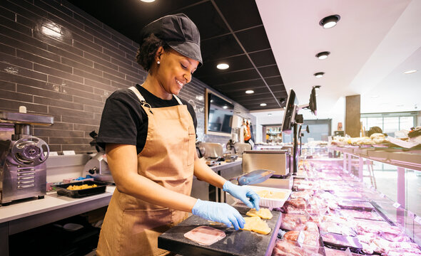 Young butcher preparing meat for sale in a modern supermarket butchery department - Powered by Adobe