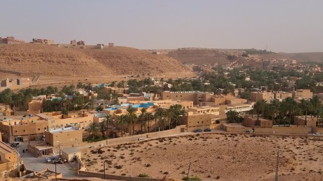 Panoramic view over Ghardaia&rsquo;s outskirts in Algeria: traditional mud-brick homes, palm trees, and rolling desert hills reflect the charm of this Saharan oasis town