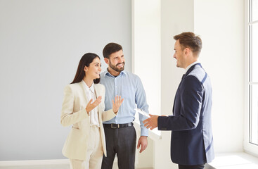 Realtor or real estate agent showcases a new apartment or house to a young happy family couple,...