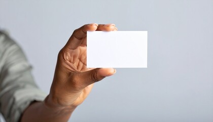 Obraz premium Mano de mujer sosteniendo una tarjeta blanca sobre fondo gris