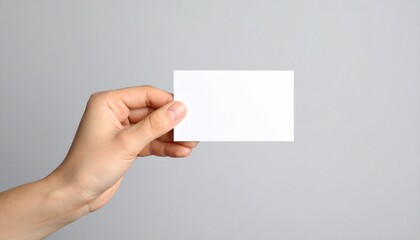Obraz premium Mano de mujer sosteniendo una tarjeta blanca sobre fondo gris