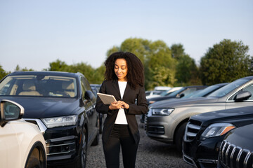 A woman in a suit is smiling while using a tablet in a car dealership.