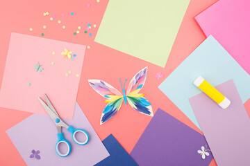 Color paper butterfly craft with glue and scissors on pink background, useful for educational...