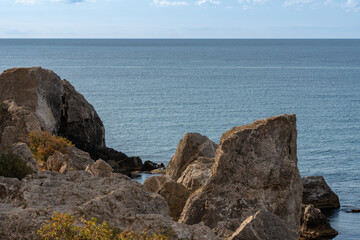Rocky coast of Black Sea. Coastal scene with steep cliffs and large boulders of Cape Alchak rises above calm waters of Black Sea under clear blue sky. Velvet season in Sudak in Crimea