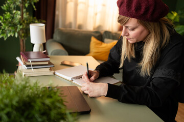 Woman writer taking notes in notebook at home office desk working on new book manuscript