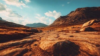 Fototapeta premium A rocky path winds through a high-altitude mountain valley, bathed in golden sunlight