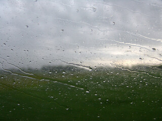 Rainy day view through a window with water droplets and streaks, revealing a blurred landscape of...