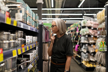 Stylish mature woman selects home goods at a large home improvement store while contemplating her...