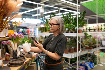Stylish mature woman shopping for home goods at a modern retail store, selecting decor and plants in a vibrant environment