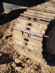 Close-up of excavator caterpillars on rough terrain, showcasing detailed treads and dirt accumulation. Ideal for construction and machinery themes.