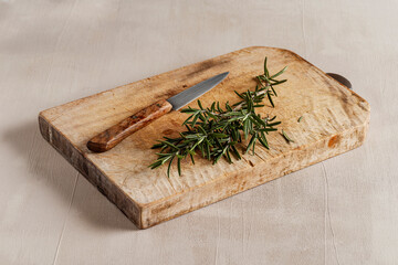 Group of fresh rosemary sprigs arranged on a wooden cutting board, set against a light background that enhances their deep green color.