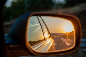 Sunset reflection in the rearview car mirror. Sun, highway car road reflection in mirror. Trip, summer holidays trip concept.