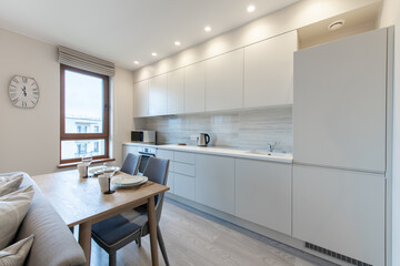 Classic White Kitchen Interior and Dinning Table. Oven, Kettle, Microwave and Glass. Plates on the Table. Minimalistic Interior Design