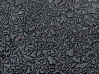 Close-up of a textured black surface with intricate, irregular patterns resembling cracks or veins,...