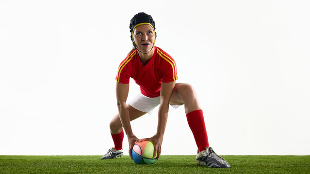 Rugby athlete in red attire stands ready with vibrant ball on green field. Concept of ball pickup, play start, concentration moment, pre-action pose, tension build and sports ritual - Powered by Adobe