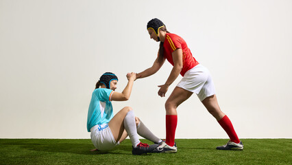 Female rugby athlete helping another to get up on grassy field in match. Concept of team support,...