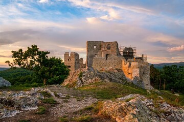 Obraz premium Medieval building illuminated by the setting sun and blue sky with clouds. Ruins of Hrusov Castle, an ancient feudal castle located in West Slovakia near city Nitra. History old Hungary and Austria.