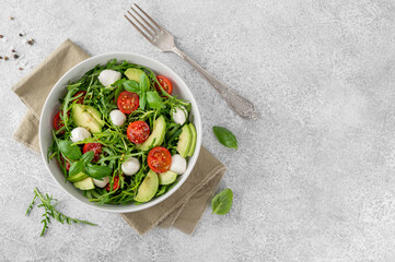 Fresh salad with arugula, mozzarella, tomatoes and avocado in a bowl. Healthy vegetarian dish.
