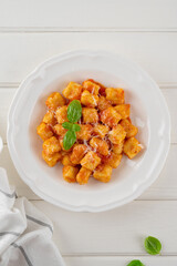 Traditional potato gnocchi with tomato sauce, parmesan cheese and fresh basil on a plate on a white wooden background. Italian cuisine. Top view, copy space.