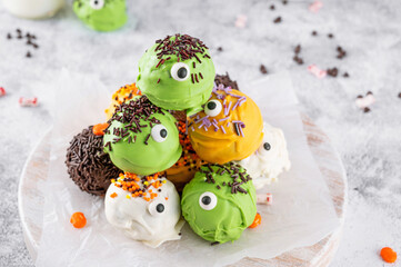 Homemade funny monster mini cakes or cake pops in a colored chocolate glaze and sugar sprinkles....