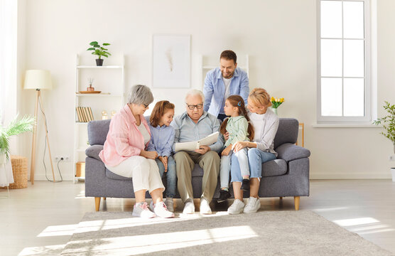 Large happy family bonding at home living room, gathering together and enjoying memories by looking through a photo album on the sofa. Love, remembrance, and strong family bonding.