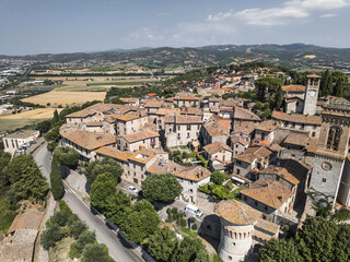 Aerial view of sun-kissed terracotta roofs cascade down the gentle slopes, ancient stone buildings clustered around the towering clock tower, Corciano, Umbria, Italy.
