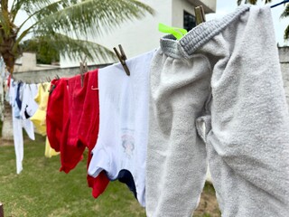 Roupas infantis coloridas a secar no varal num quintal tropical. Uma cena cotidiana, simples e familiar, com uma atmosfera de calor e vida doméstica.