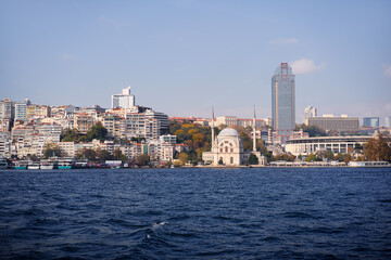 Fototapeta premium Serene waterfront view showcasing historic monuments, modern buildings, and vibrant cityscape along the Bosphorus, under a clear sky. View of Bosphorus Waterfront with Historic and Modern Architecture