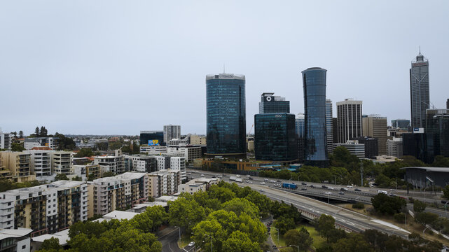 Perth, Australia - 29 November 2024: Aerial view of modern skyscrapers piercing the skyline, contrasted by lush green parks and residential buildings below, all under a diffused light.