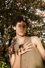 Curly-haired young man showcases summer fashion in lush green park setting