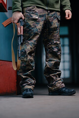 A close-up image of a person in military camouflage standing with a rifle. The focus on details...