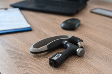 Wrist expander lying on table in modern office, closeup photo. Modern tonometer on wooden desk with...