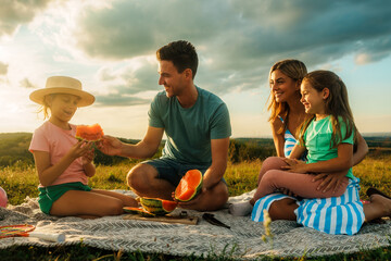 Happy family eating watermelon in nature while having family bonding time before school starts in...