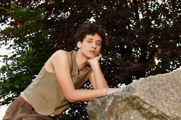 Curly-haired young man embraces summer style while enjoying nature in a vibrant park