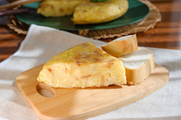 Spanish omelette slice with bread on wooden board in sunlight