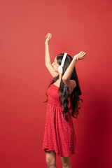 young woman dancing with headphones arms up red dress on red background vertical
