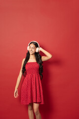 young woman enjoying music eyes closed smiling with headphones red dress red background vertical