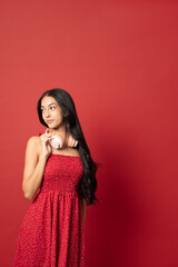 young woman holding headphones around neck looking away in red dress against red background vertical