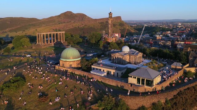 Aerial video of Calton Hill at Sunset with people socialising and Holyrood park hills on the background. 