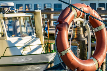 Bright sunny day on a fishing boat with a ship's bell and life buoy prominently displayed,...