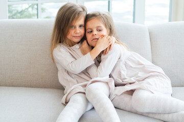 Happy family sisterly love. Two funny little twin sisters girls hugging with love care playing together at home indoors. Happy children lifestyle. Identical twin girls hugs. Girls friendship and youth