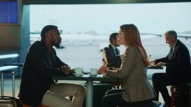 Two business people conversing over coffee at an airport, with the airport in the background.