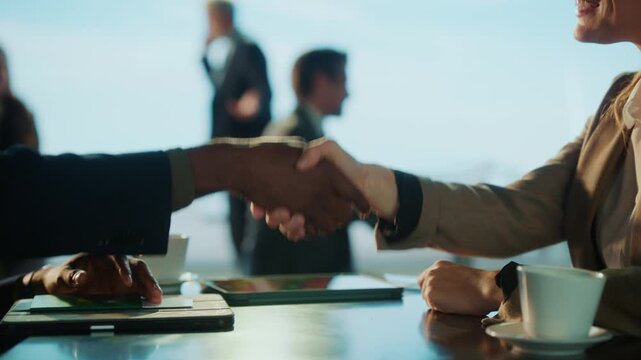 A business deal is sealed with a handshake. Diverse individuals in suits are present, suggesting a professional setting.