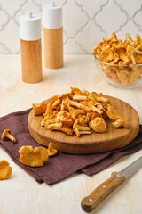 Fototapeta premium Fresh chanterelles on a round wooden board on a light concrete background. Wild mushrooms, gifts of the forest.