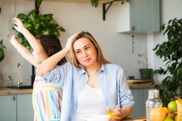 Young woman mom sitting on a kitchen table looking stressed suffers from headache because of noise...