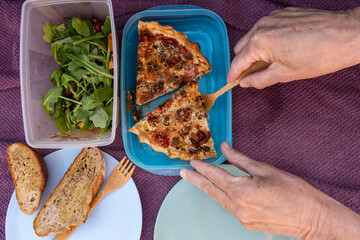 Stockholm, Sweden Hands serve a piece of homemade quiche onto plastic plates and a salad.