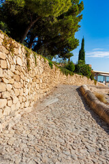 A serene cobblestone path lined with a rustic stone wall and greenery, leading visitors through a...