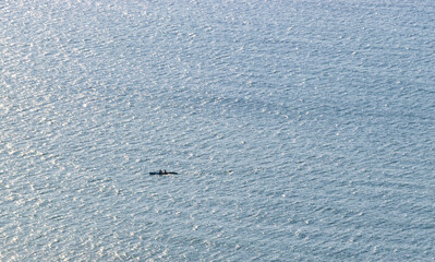 A serene view of two people kayaking on a calm ocean surface, showcasing shimmering reflections of sunlight on the water during a clear day.