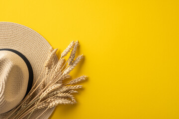Straw hat and wheat stalks arranged gracefully on bright yellow background evoking summer